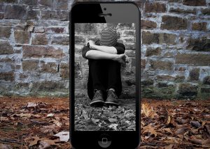 teen with head down sitting against a wall. Framed in a cell phone screen.