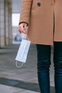 person in brown coat and black pants holding a paper mask