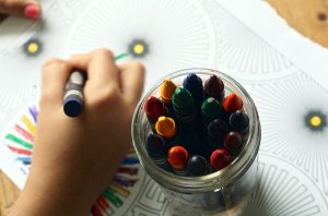 child with jar of color crayons coloring on white paper